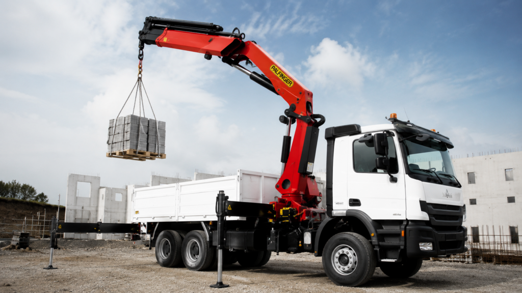 Camion équipé d’une grue PALFINGER en action sur chantier pour le levage et la manutention de matériaux.